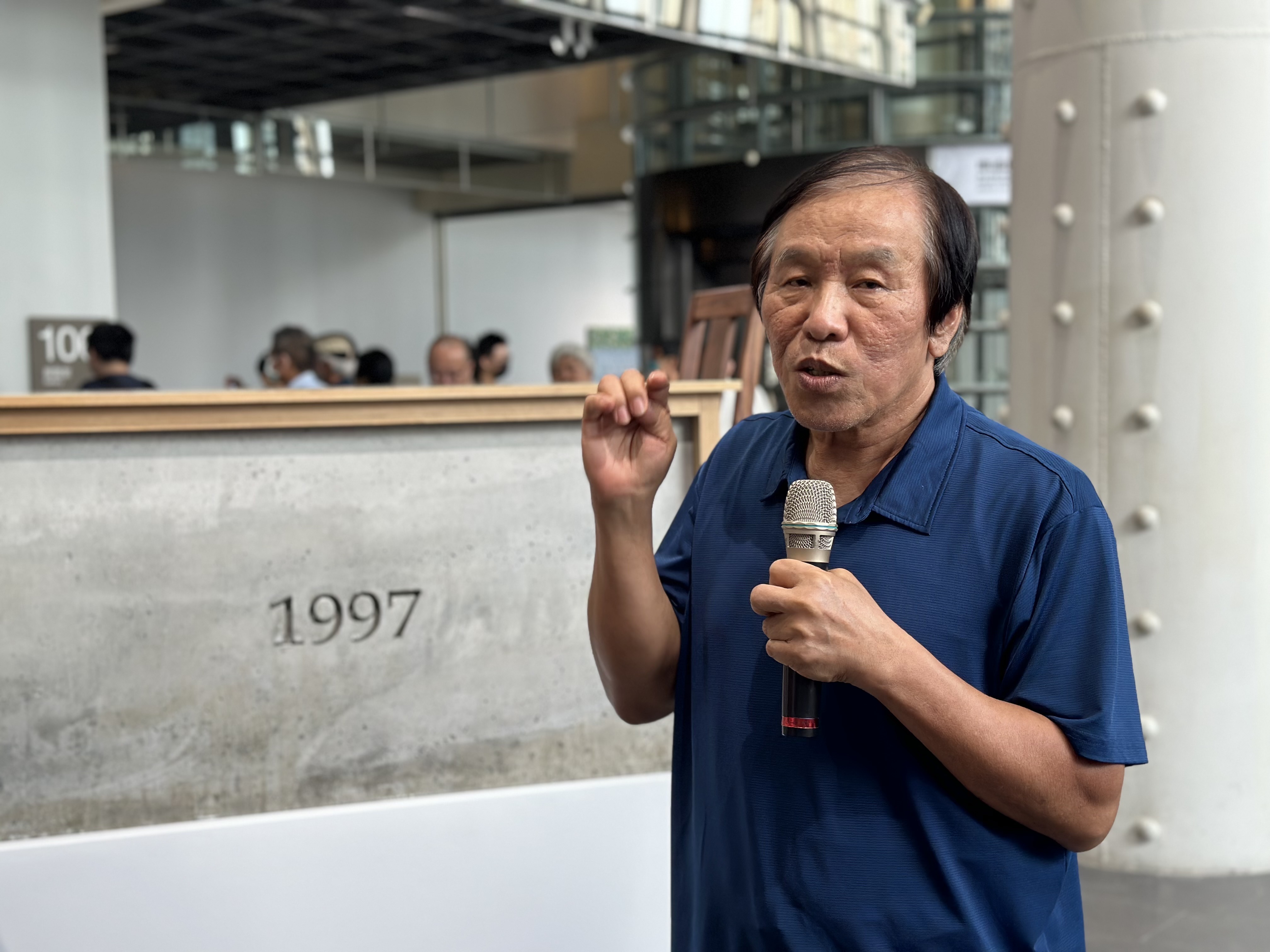 策 展 人 石 瑞 仁 於 展 場 導 覽 ， 身 後 作 品 為 莊 普 ， 1 9 9 7 紀 念 碑 ， 1 9 9 6 ， 水 泥 、 木 桌 椅 、 展 台 ， 國 美 館 典 藏 。 攝 影 / 戴 衣 薰 